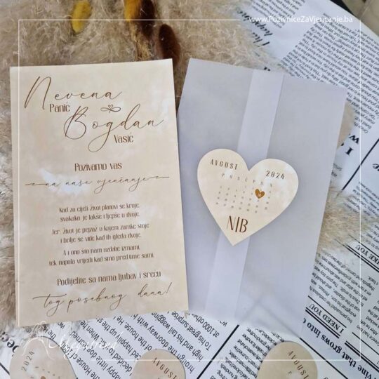 Prikaz pozivnice sa omotačem od providnog papira i karticom u obliku srca. Papir na kojem je odštampan tekst ima štampu sa obje strane, a kartica koja je zalijepljena za omotač na sebi ima kalendar za mjesec u kojem se održava događaj sa označenim danom vjenčanja.